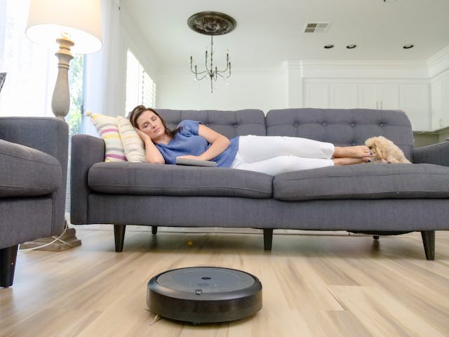 Woman sleeping on sofa while robot vacuum cleans.