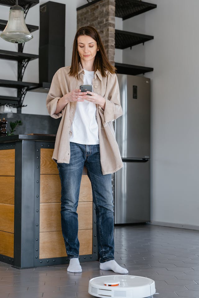 Woman with robot vacuum at her feet.