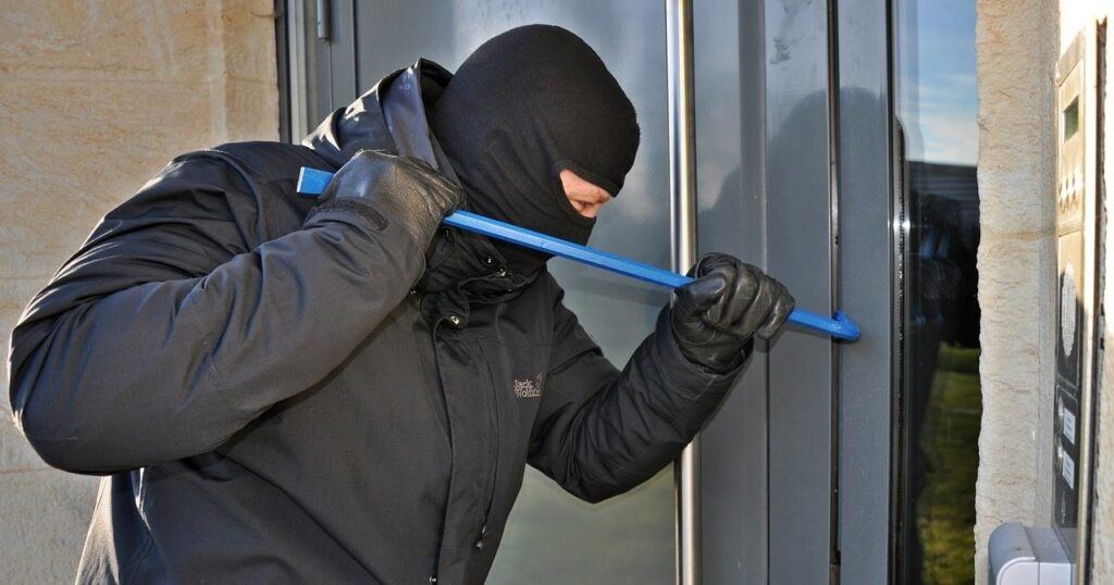 Burglar prying door open with crowbar.